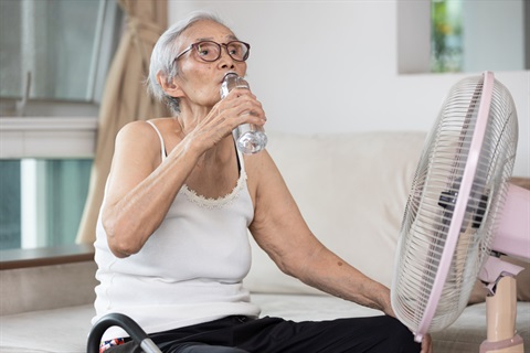 Elderly women drinking water in front of fan during heatwave