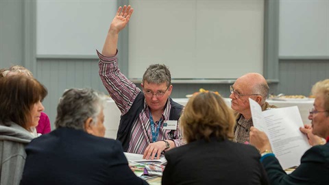 older person with hand up in meeting