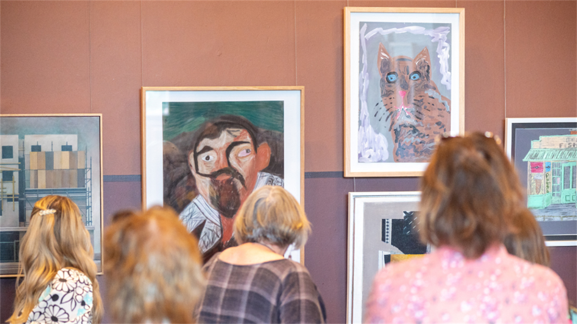 A group of people view salon hung artwork on a wall