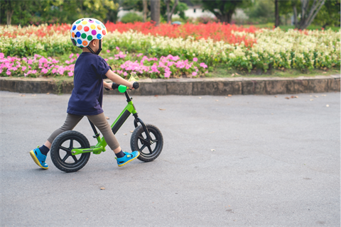 child riding a scooter on path in front of flower bed.png