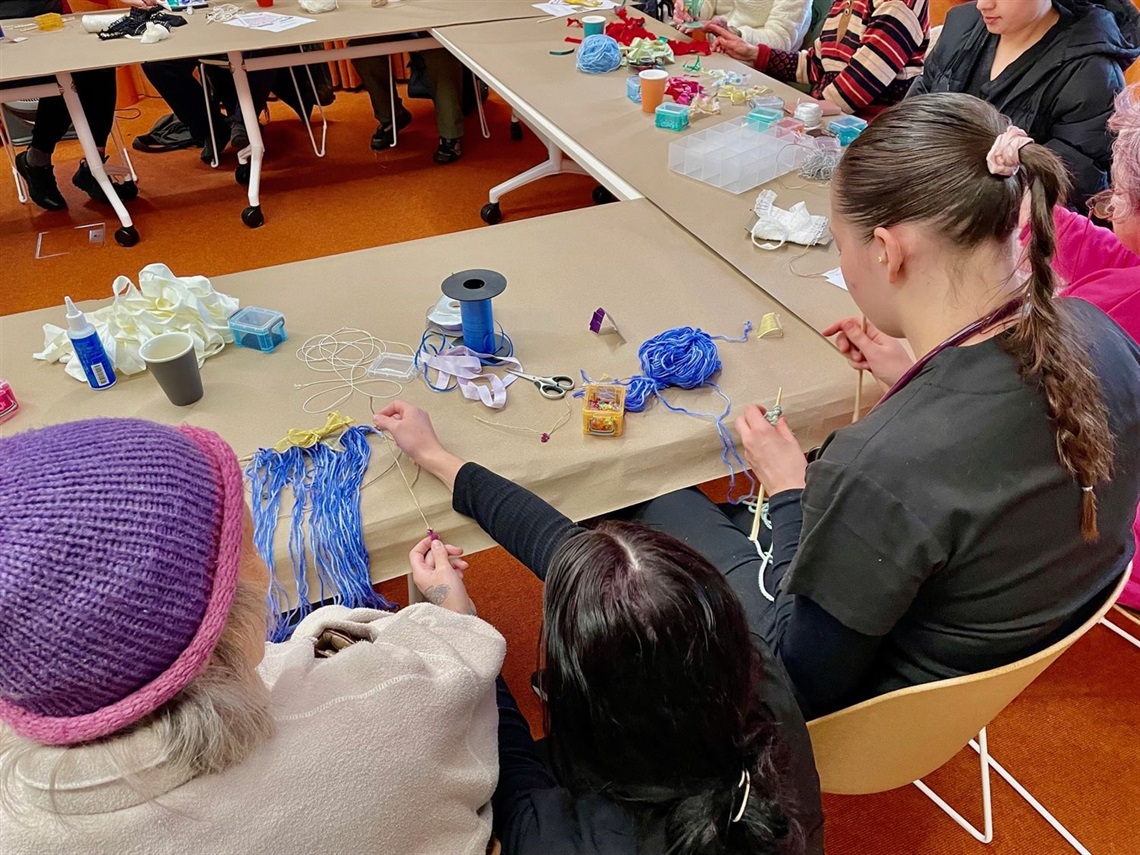 People sitting at tables doing art and craft activities involving string, yarn and ribbons.jpg